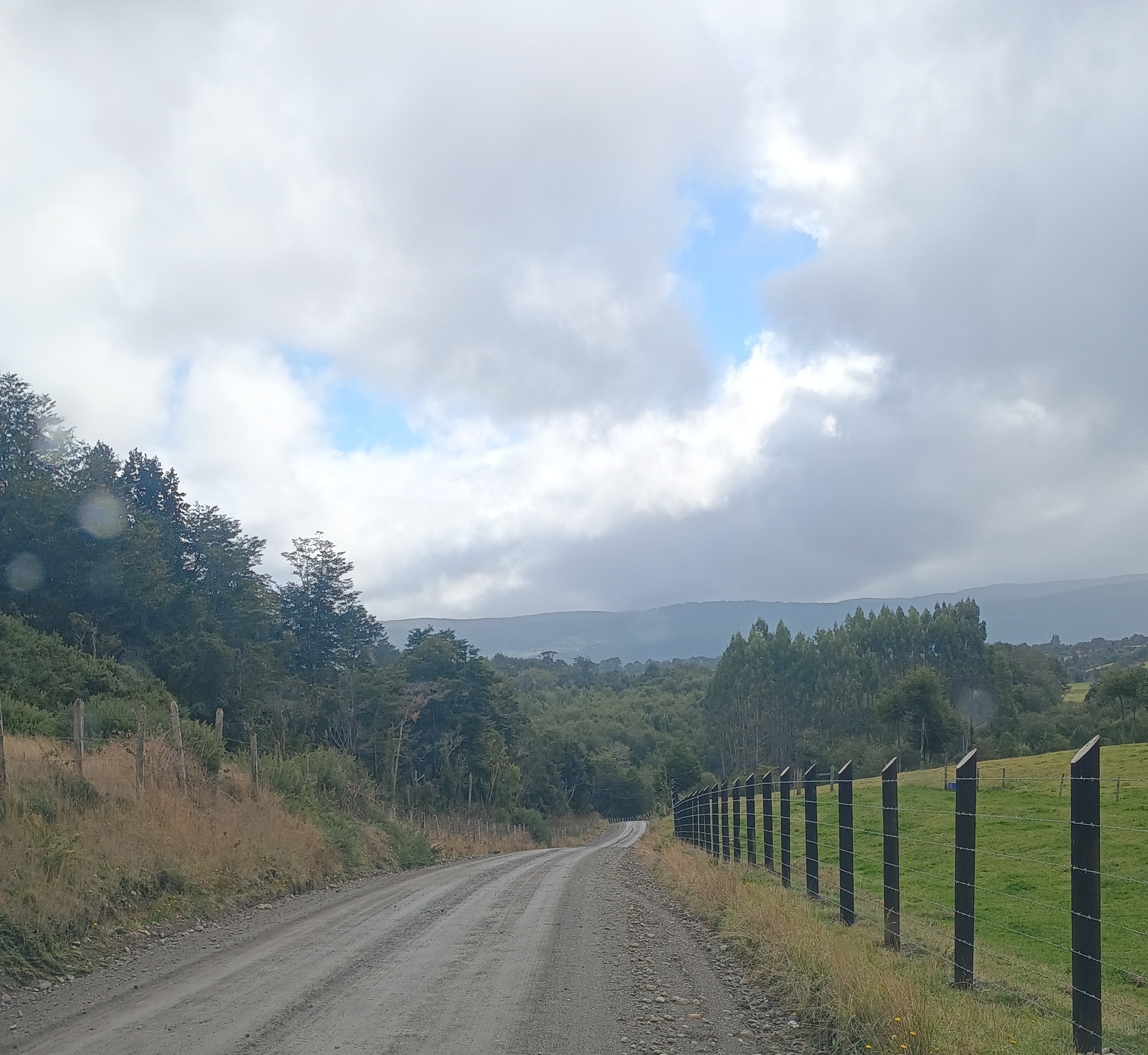 Camino rural con cercos y bosque nativo hacia la cordillera de Chiloé